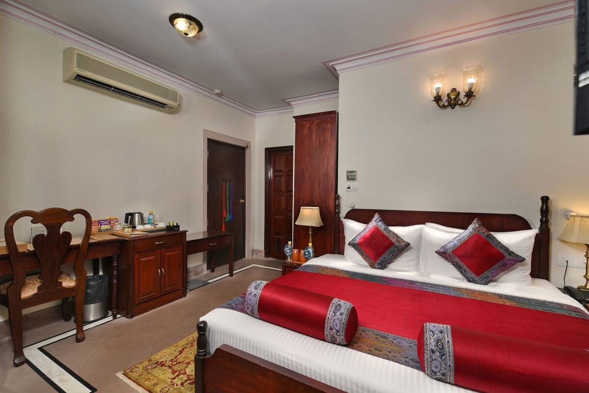 A hotel room with a bed, desk, chair, and a wall-mounted air conditioner.