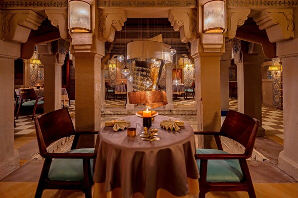 A dining area with a round table, two chairs, a candle centerpiece, and ornate wall decorations.