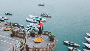 A person standing on a circular platform with potted plants, overlooking a marina with several boats. - BrijRama Palace, Varanasi - By the Ganges (Varanasi)