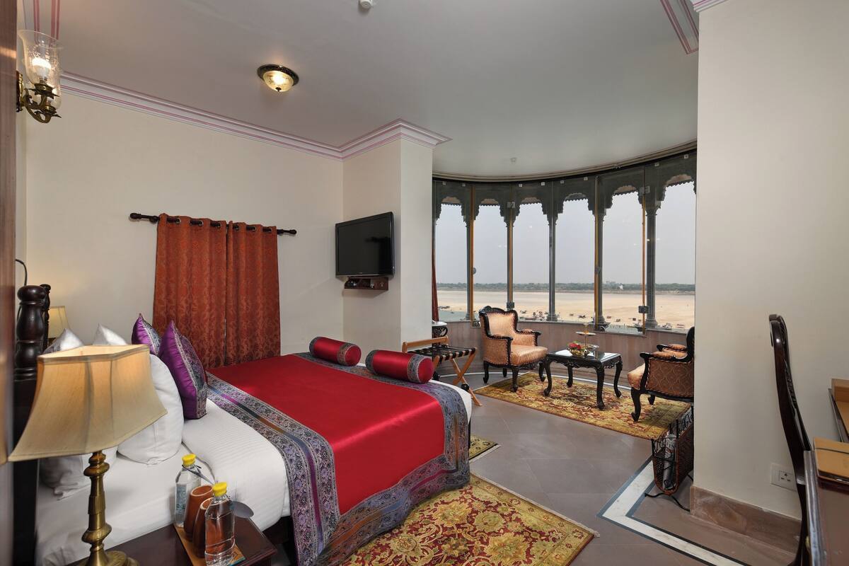 A hotel room with a large bed, a TV, a balcony with a view of the beach, and a seating area with a table and chairs.