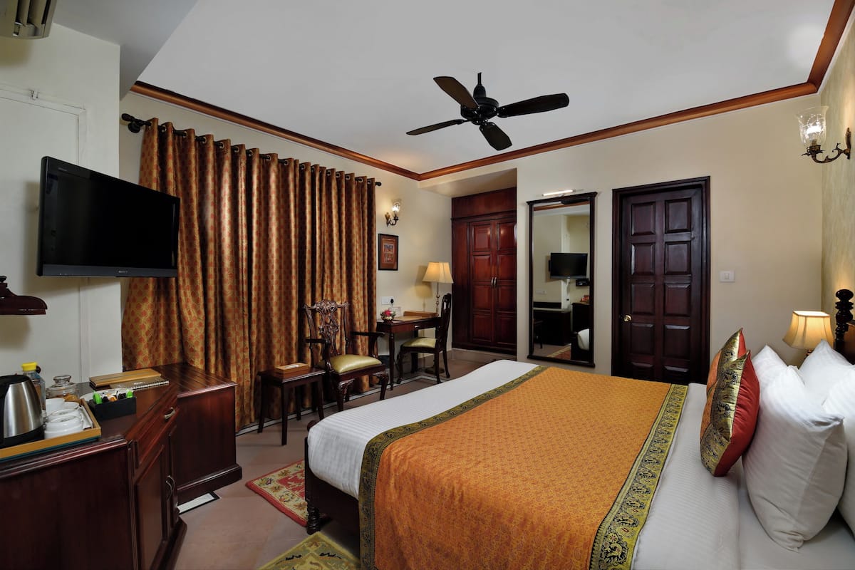 A hotel room with a bed, a desk, a chair, a television, a ceiling fan, and a wardrobe.