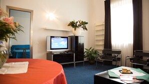A hotel room with a bed, a television, a desk with a chair, a potted plant, and a window with curtains. - Residence Hotel Castelvecchio (Verona)