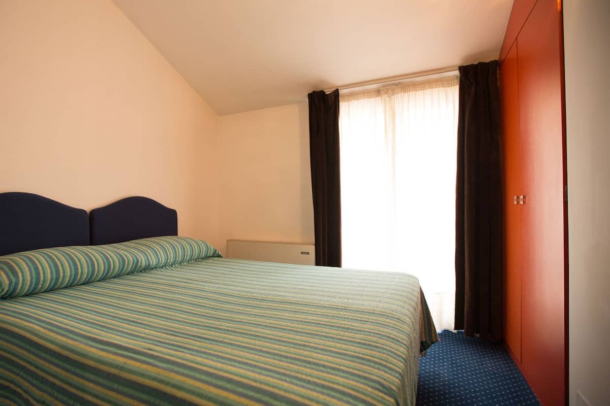 A hotel room with a bed, a window with curtains, and a door.