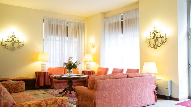 A living room with a sofa set, a round table with a vase of flowers, and two lamps. - Residence Hotel Castelvecchio (Verona)