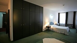 A hotel room with a large wardrobe, two beds, a bedside table with a lamp, and a view of the outdoors through the window. - Residence Hotel Castelvecchio (Verona)