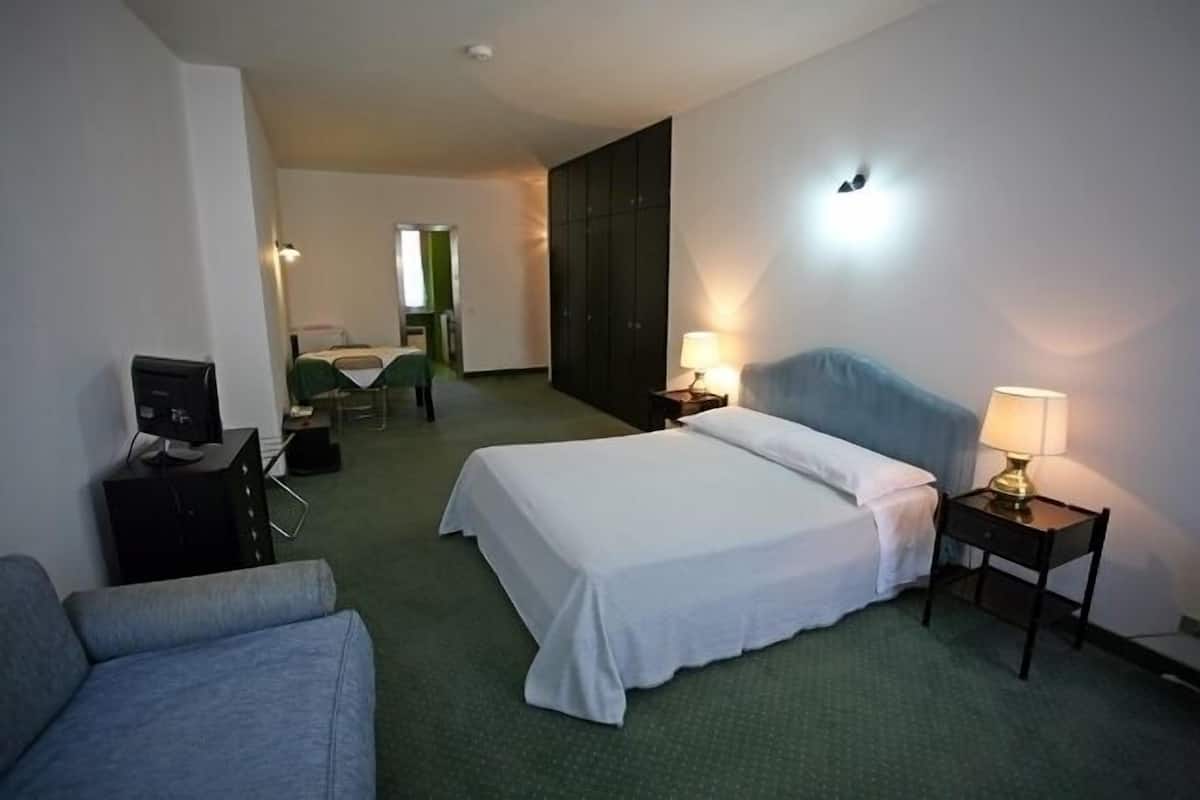 A hotel room with a single bed, a desk with a computer, a chair, and a lamp.