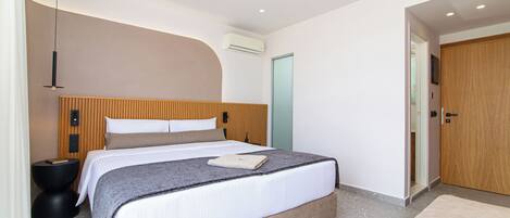 A modern bedroom with a large bed, a bedside table, an air conditioning unit, and a wooden door.