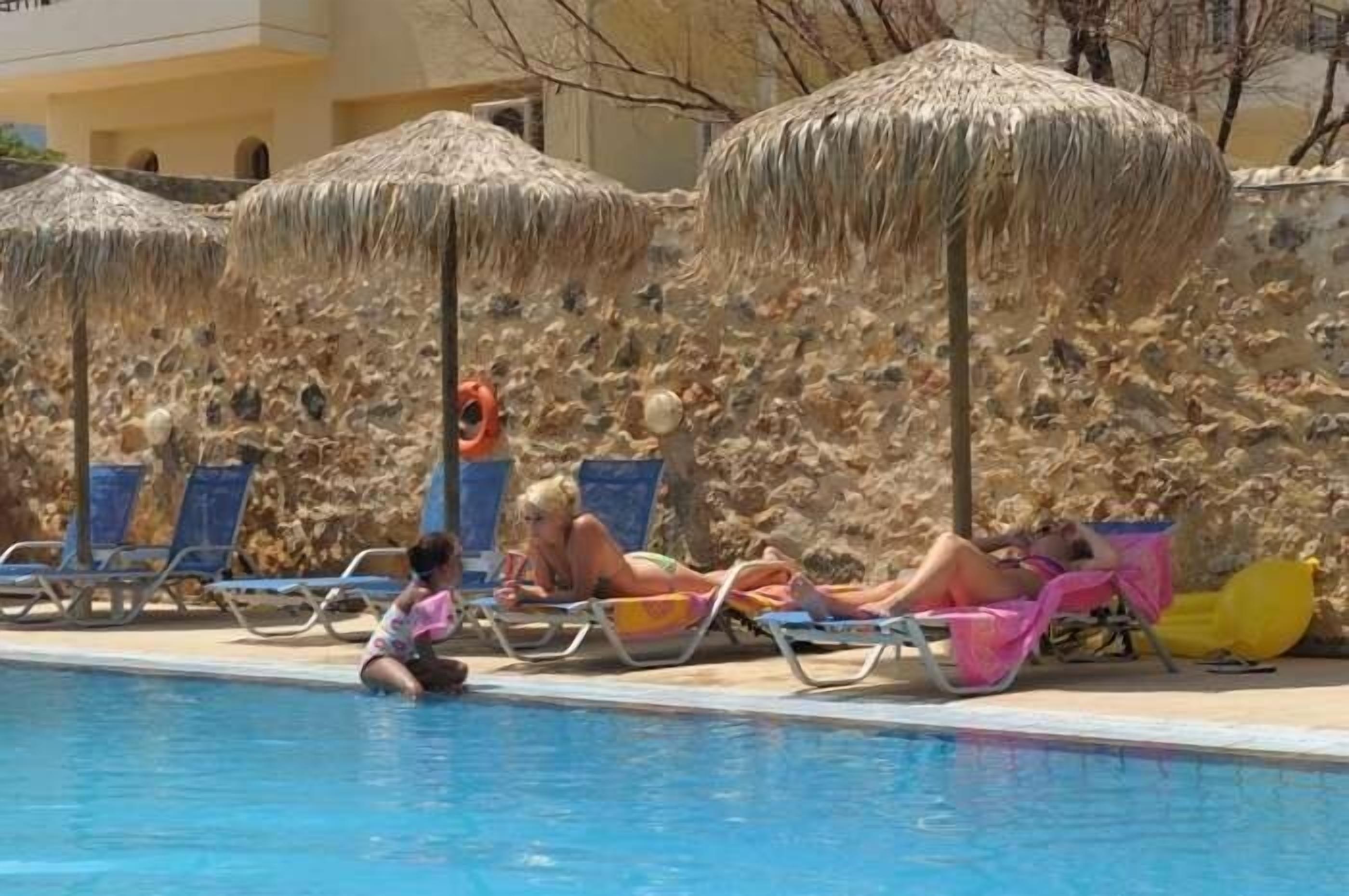 Un área junto a la piscina con sillones de descanso y sombrillas de paja.