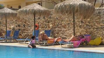 Un área junto a la piscina con sillones de descanso y sombrillas de paja.