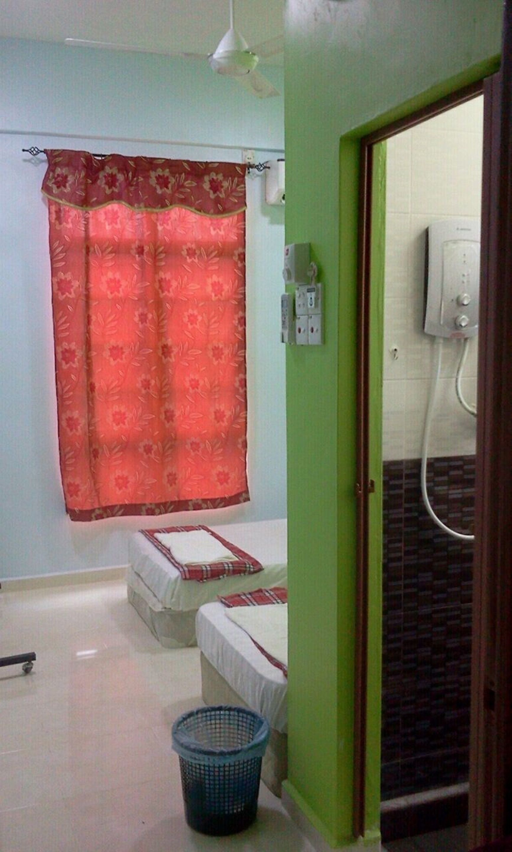 A small, simple bathroom with a shower, a toilet, and a bed with a red and white bedspread.