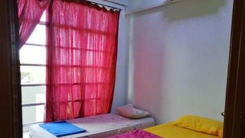 A small room with a bed, a window with red curtains, and an air conditioning unit on the wall.