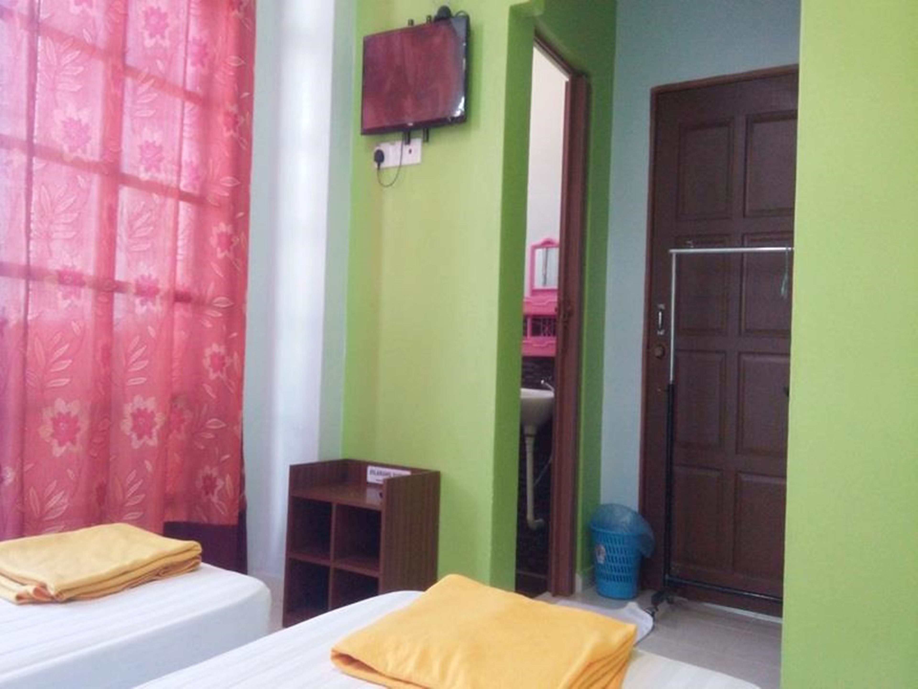 A room with two beds, a wooden cabinet, a blue laundry basket, and a door.