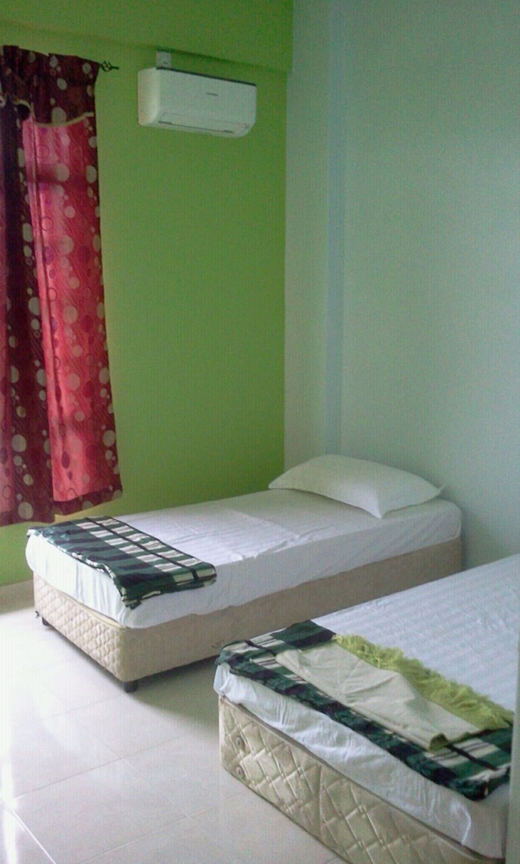 A room with two beds, a red curtain, and an air conditioning unit on the wall.