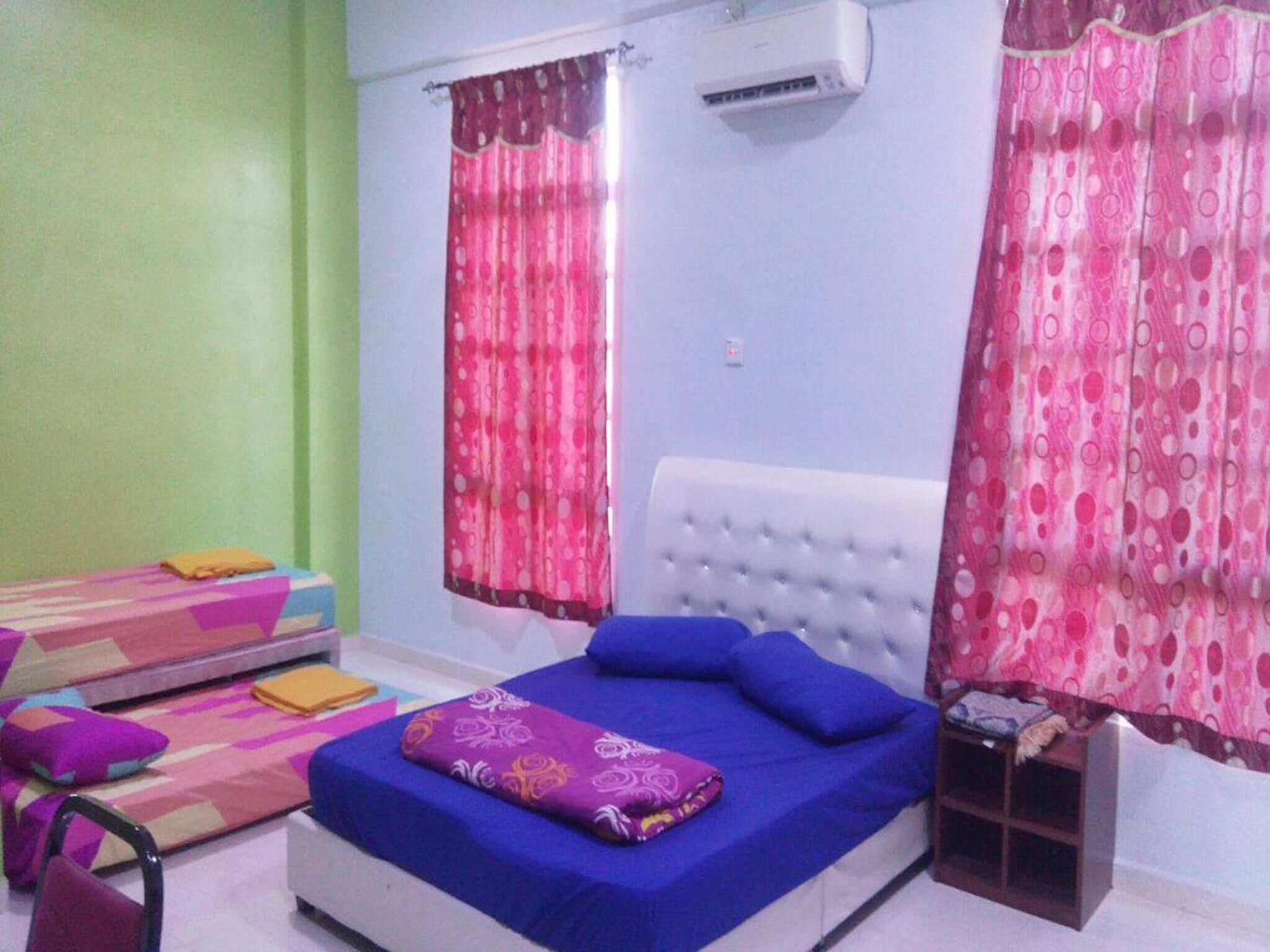 Un dormitorio con cama, mesita de noche, silla, ventana con cortinas y aire acondicionado.