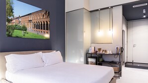 A modern hotel room with a large bed, a desk with a computer, a mirror, and a view of a historic building. - BC MAISON bed&cafe Milano (Milan)
