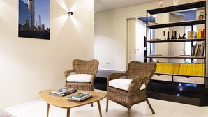 A modern living room with two wicker chairs, a wooden coffee table, and a bookshelf filled with books and decorative items. - BC MAISON bed&cafe Milano (Milan)