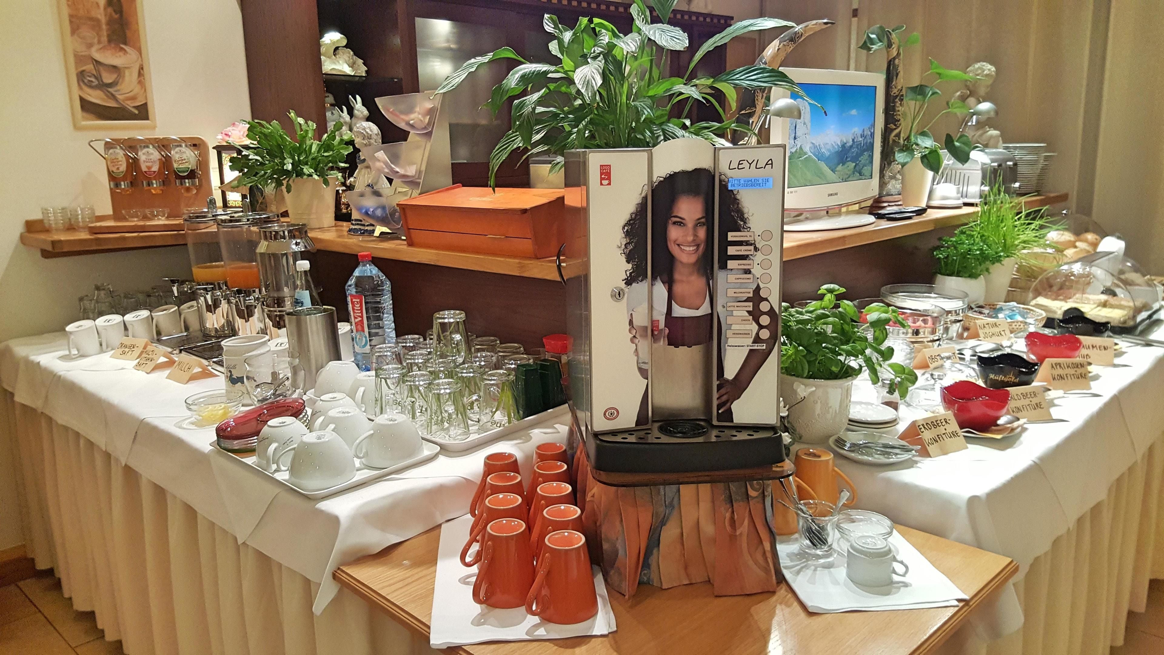 A buffet setup with various food items, a coffee machine, and a computer monitor on a table.