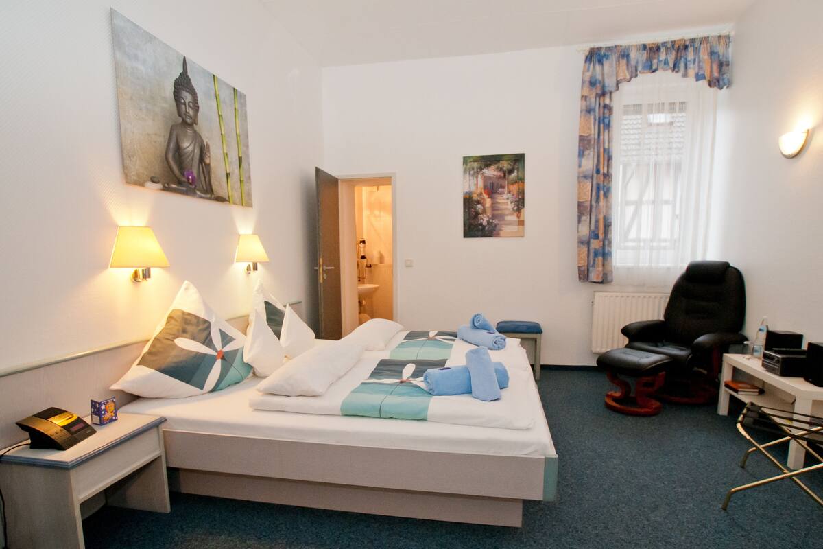 A hotel room with a bed, two bedside lamps, a chair, a desk, and artwork on the walls.