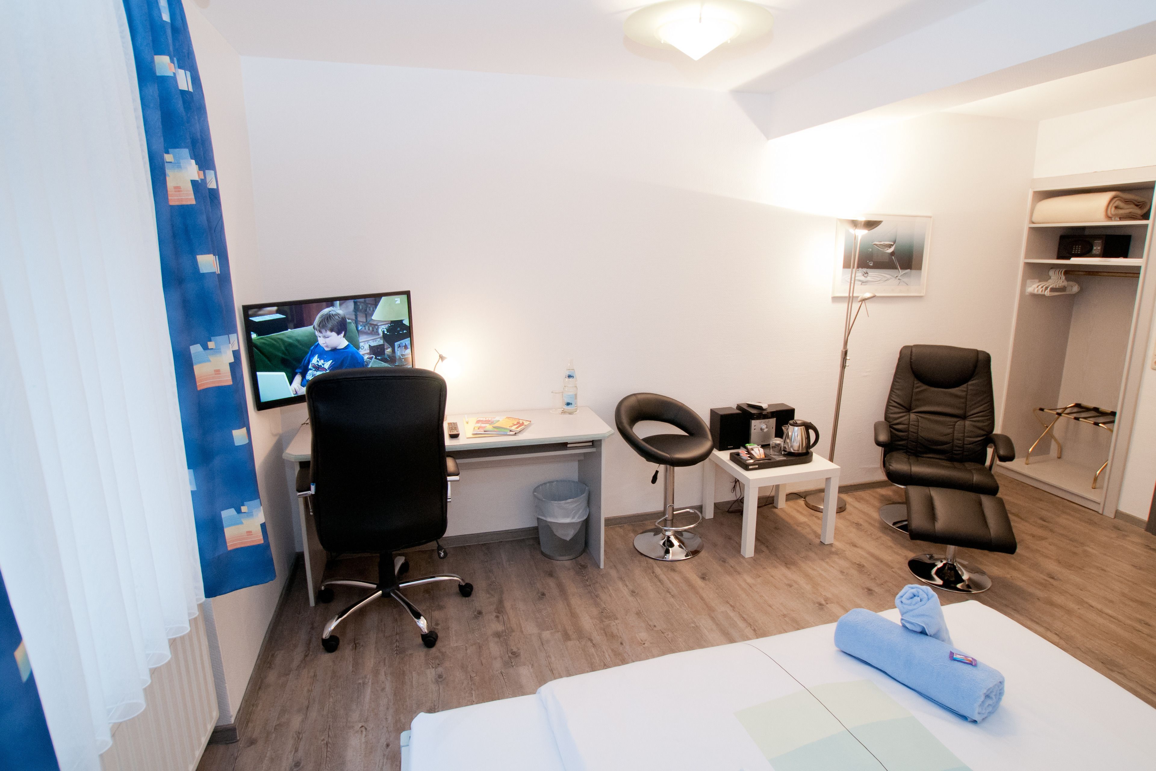 Ett hotellrum med en säng, ett skrivbord med en dator, en stol, ett litet bord och en garderob.