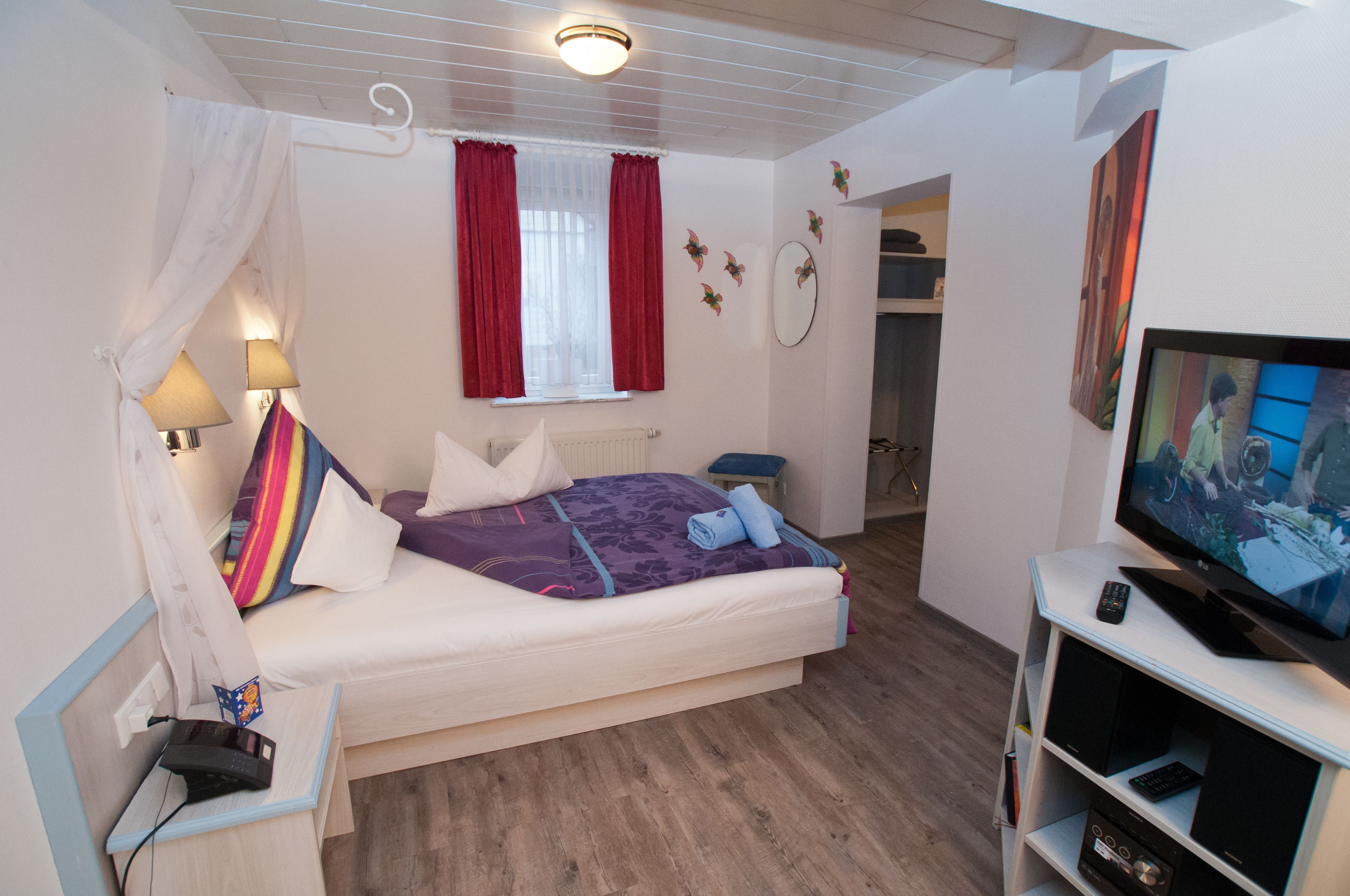 A bedroom with a bed, a TV, a bedside table, a lamp, and a window with curtains.