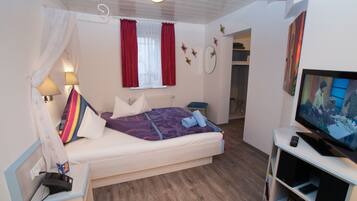 A bedroom with a bed, a TV, a bedside table, a lamp, and a window with curtains.