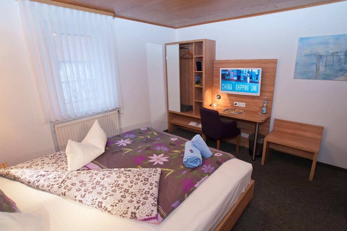 A bedroom with a bed, a desk, a chair, a wardrobe, and a painting on the wall.
