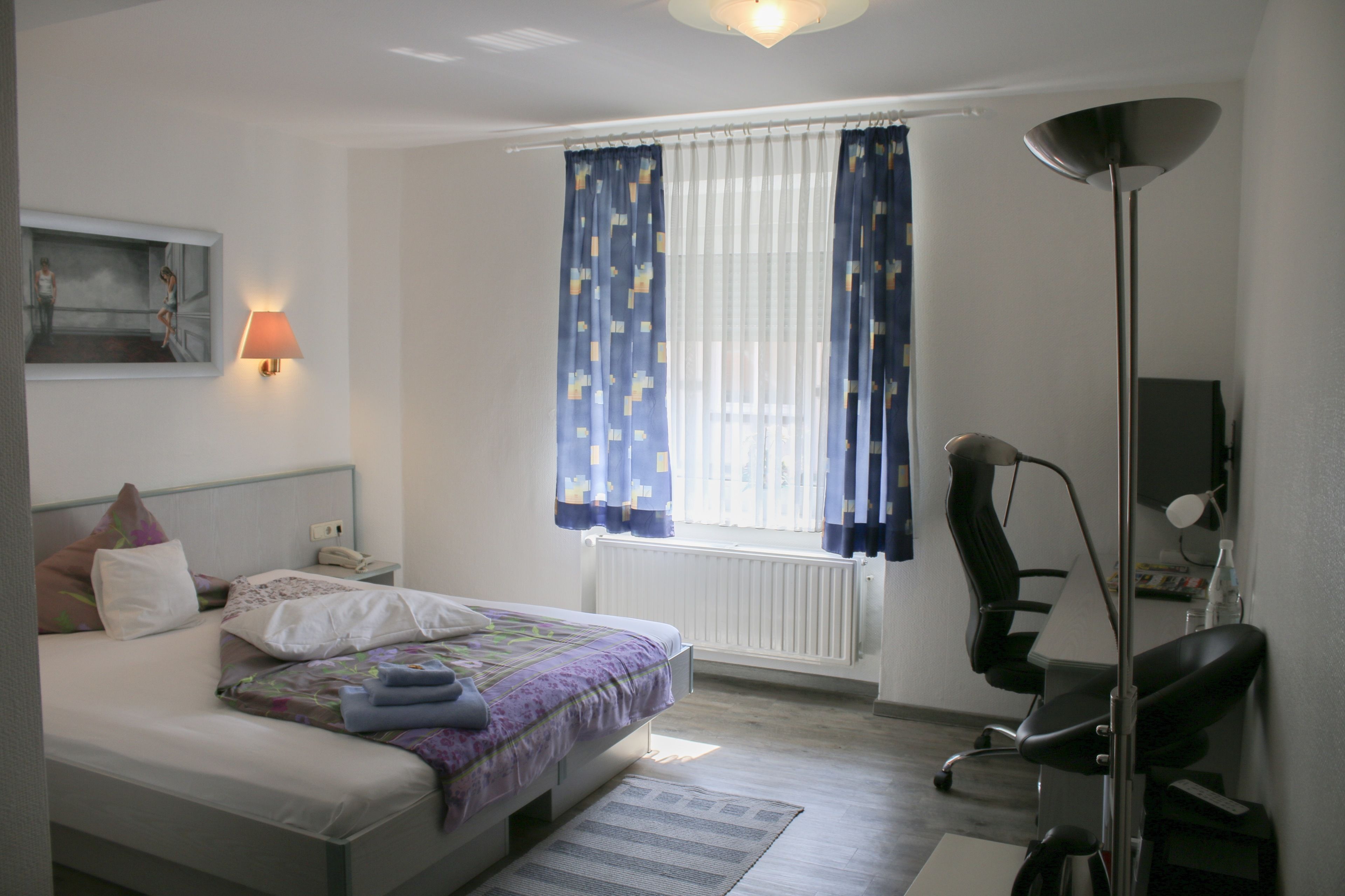A bedroom with a bed, bedside lamp, chair, and a window with curtains.
