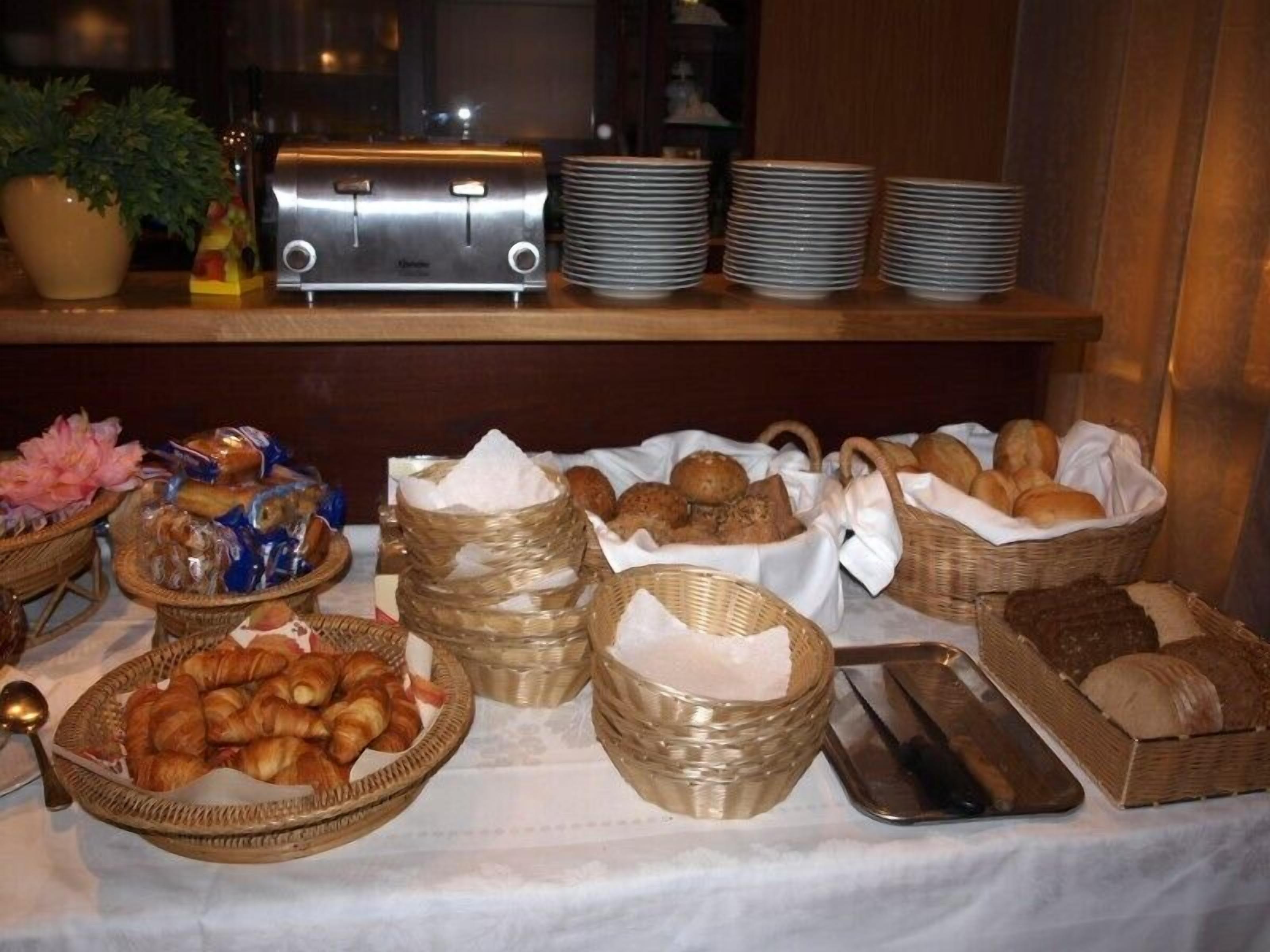 A buffet table with various food items, including baskets of bread and pastries, and stacks of plates.