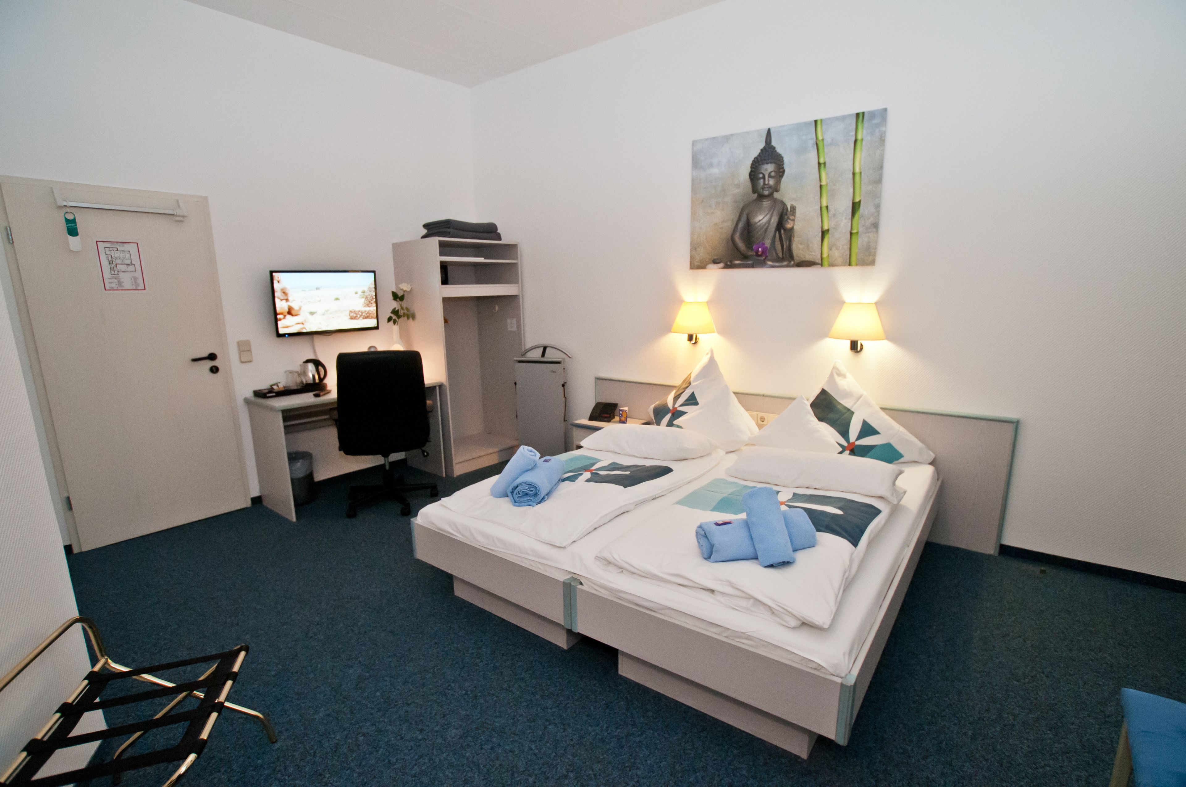 A hotel room with a bed, desk, chair, and a painting on the wall.