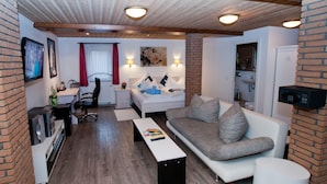 A modern living room with a sofa, coffee table, and a TV. There is a desk with a chair and a window with curtains.