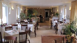A spacious dining area with multiple tables and chairs, warm lighting, and decorative plants.