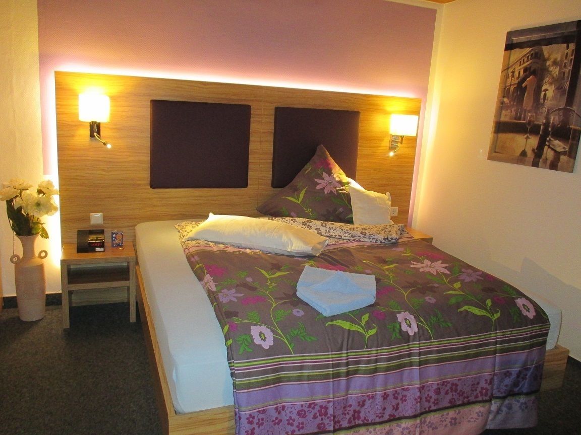 A neatly made bed with floral bedding, a bedside table with a lamp, and a wall-mounted light fixture.