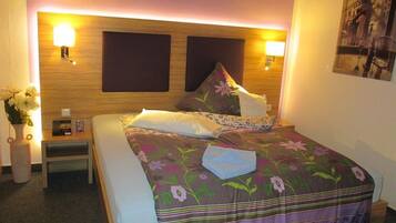A neatly made bed with floral bedding, a bedside table with a lamp, and a wall-mounted light fixture.