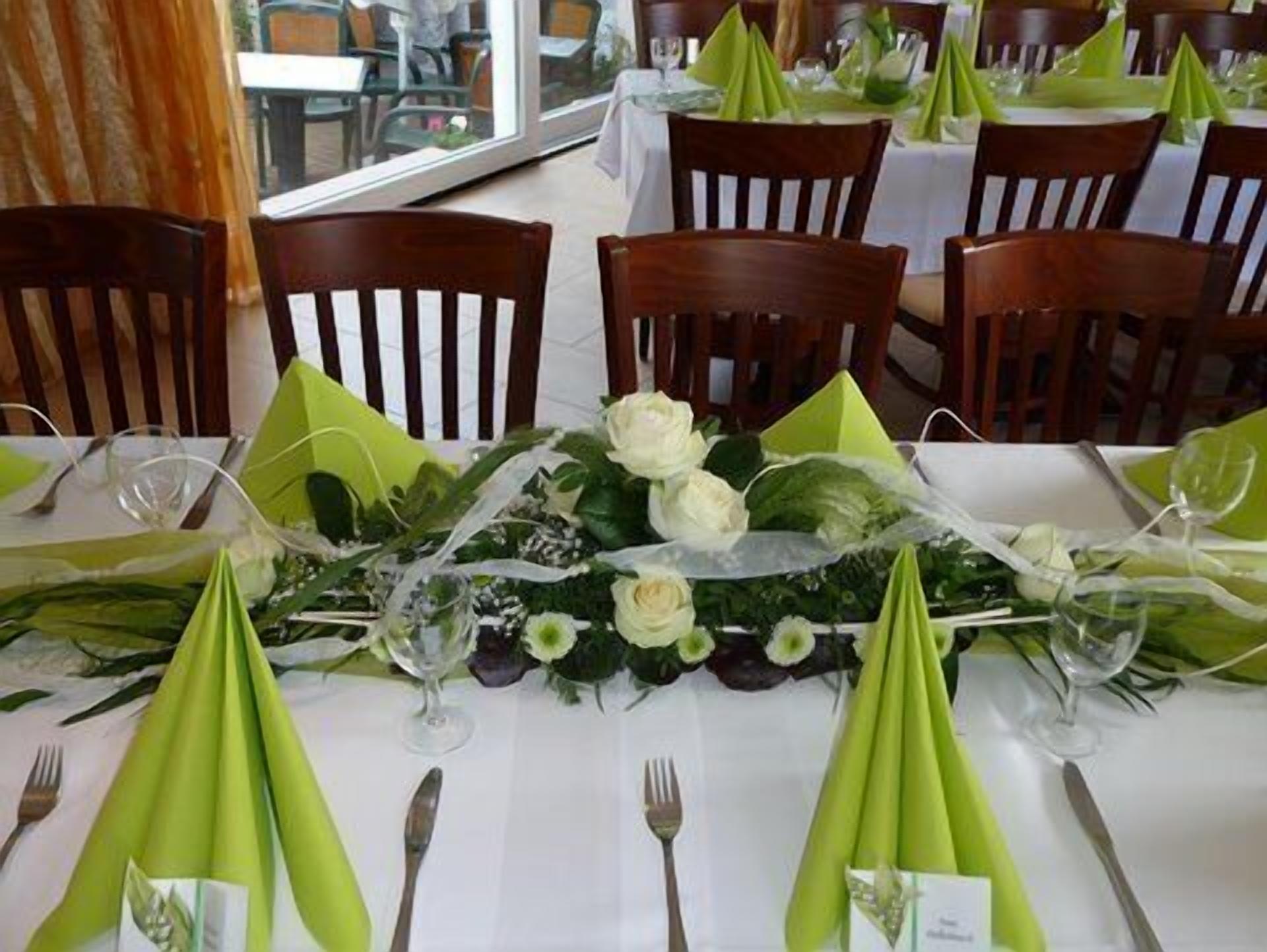 Ein Essbereich mit gedeckten Tischen, mit grünen Servietten, weißen Tischdecken und floralen Mittelstücken.