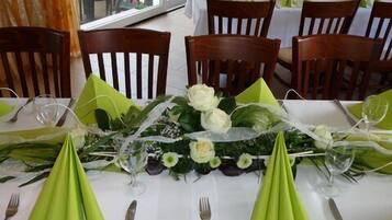 Ein Essbereich mit gedeckten Tischen, mit grünen Servietten, weißen Tischdecken und floralen Mittelstücken.