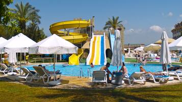 Relax by the pool with lounge chairs and umbrellas, surrounded by lush greenery and a spiral water slide.