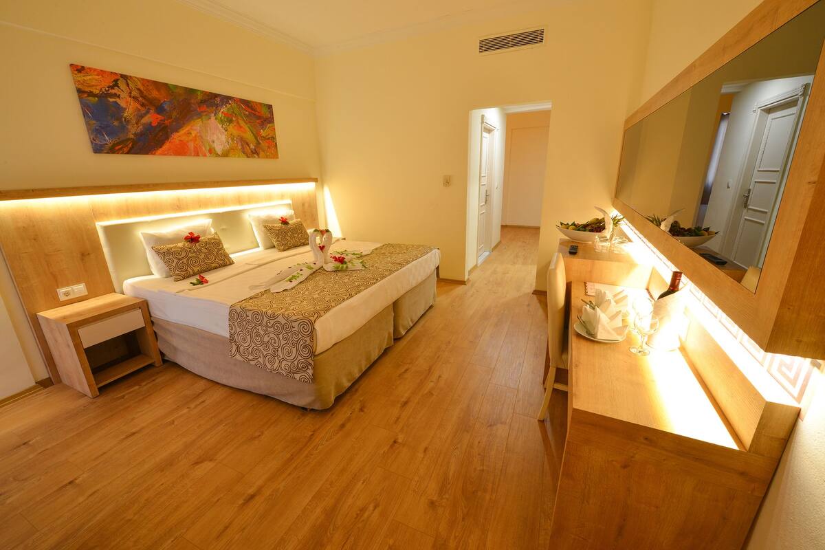A bedroom with a large bed, bedside tables, a mirror, and a wooden floor.