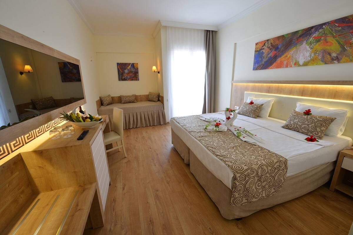 A hotel room with a large bed, a desk with a mirror, a sofa, and a large abstract painting on the wall.