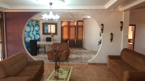 A living room with two sofas, a coffee table with a giraffe figurine, a dining area with a marble table, and a large window with curtains. - Tribeca Hotel Annex (Koforidua)