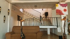 A living room with a brown sofa, two giraffe sculptures, a staircase, and a flower painting on the wall. - Tribeca Hotel Annex (Koforidua)