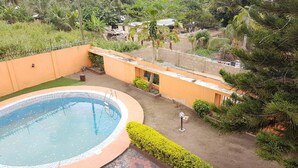 A swimming pool surrounded by a low wall and a paved area with a small garden. - Tribeca Hotel Annex (Koforidua)