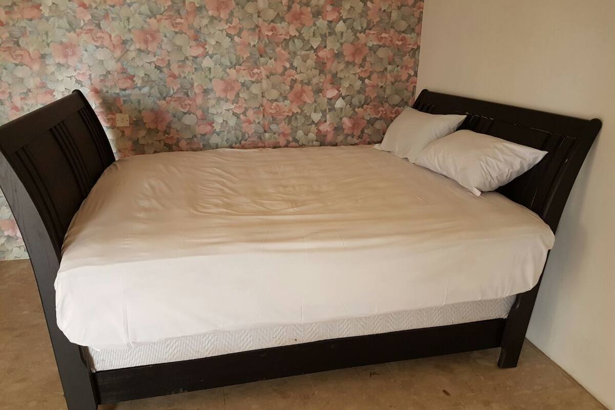 Una cama con papel tapiz estampado con motivos florales, un cabecero de madera oscura y un colchón blanco.