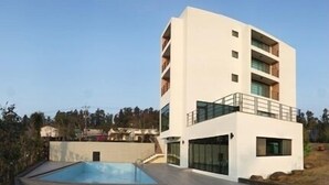 A modern multi-story building with a swimming pool in the foreground. - Suave Hotel (Seogwipo)
