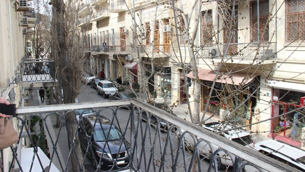 A narrow street with buildings on both sides, a pedestrian, and parked cars. - Fountain Square Hotel (Baku)