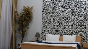 A bedroom with a bed, a nightstand, a lamp, a potted plant, and a patterned wallpaper. - Fountain Square Hotel (Baku)