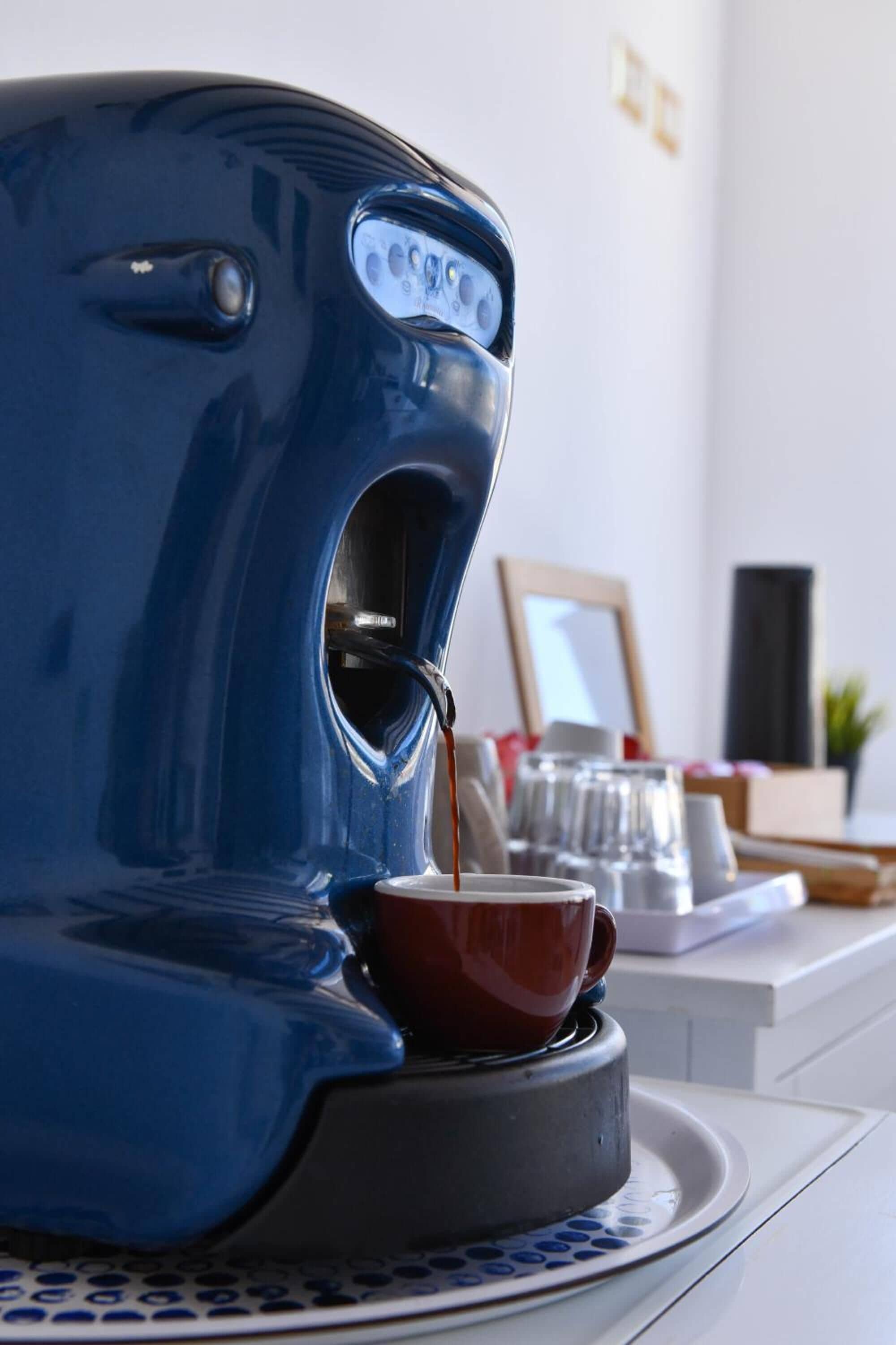 A blue coffee maker dispensing coffee into a red cup on a white tray.