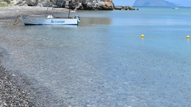 A boat named 'Blu Lounge' anchored near a rocky coastline with clear water and a distant mountain. - Mamamia Guesthouse (Lipari)
