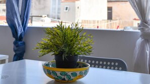 A balcony with a table, a potted plant, and a view of a building with a tower. - Mamamia Guesthouse (Lipari)