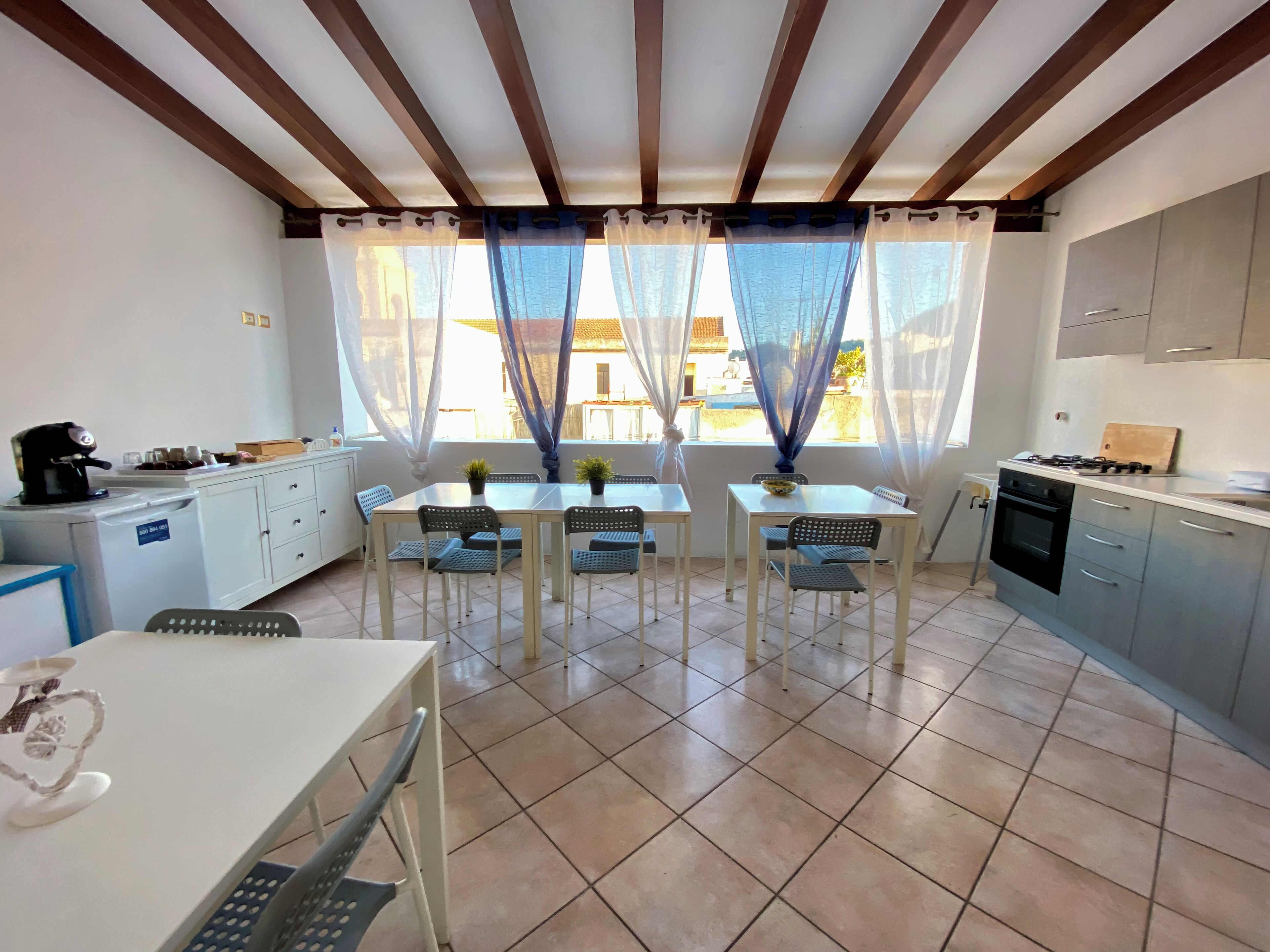 A kitchen with a dining area, featuring a tiled floor, white cabinets, a gas stove, and a coffee machine.