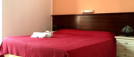 Una habitación de hotel con una colcha roja, un cabecero de madera, una mesita de noche con una planta y una pared con una cita en italiano.